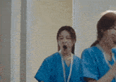two female nurses in blue scrubs are yawning in a hospital room .