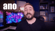 a man with a beard is sitting in front of two computer monitors and the word ano is visible