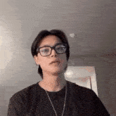 a man wearing glasses and a black shirt is standing in a room .