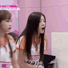 two girls are standing next to each other in front of a pink wall . one of the girls is making a funny face .