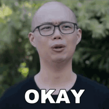 a bald man with glasses says okay in white