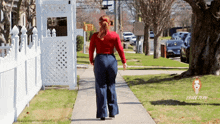 a woman walking down a sidewalk with a white fence behind her and the word little on the bottom right