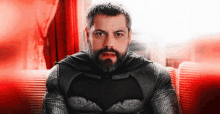 a man with a beard is wearing a batman costume and cape .