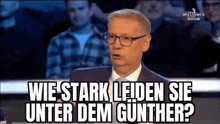 a man wearing glasses and a suit is sitting in front of a crowd and says wie stark leiden sie unter dem gunther