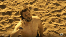a shirtless man with a beard is talking on a cell phone on the beach .