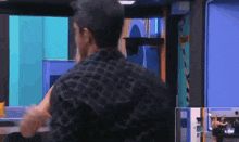 a man in a black plaid shirt is standing in a room with a blue wall .
