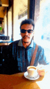 a man wearing sunglasses is sitting at a table with a cup of coffee