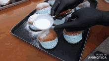 a person is adding powdered sugar to a bunch of donuts on a tray