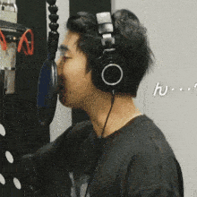 a man wearing headphones and a black shirt looks at the camera with the letter h written in white