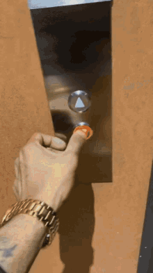 a man wearing a gold watch is pressing the elevator button