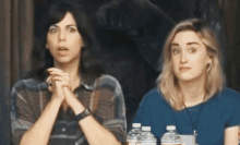 two women sit at a table with bottles of water