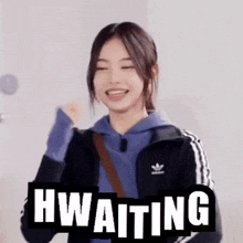 a woman wearing a blue hoodie and a black adidas jacket is smiling and holding her fist in the air .