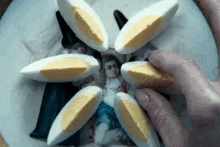 a person is holding a plate of hard boiled eggs in front of a painting of a woman .