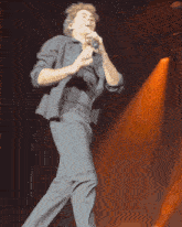 a man in a suit is singing into a microphone on stage