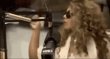 a woman is standing in front of a microphone wearing sunglasses and talking into it .
