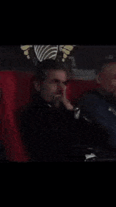 a man in a black jacket is sitting in a chair with his head down and his hand on his chin .