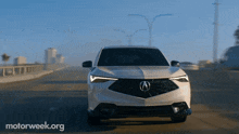 a white acura car is driving down a highway with motorweek.org written on the bottom