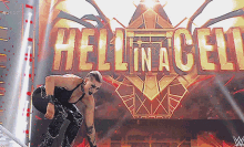 a wrestler stands in front of the hell in a cell logo