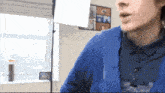 a man in a blue shirt is standing in front of a window with a picture of a man on the wall behind him