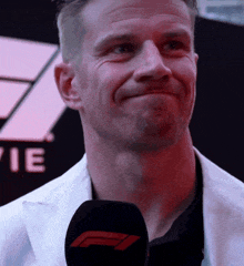 a man in a white jacket is smiling while holding a black microphone with a red f logo on it