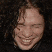 a man with curly hair is smiling with his eyes closed and his mouth open