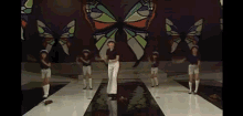 a group of people are dancing on a stage in front of a large butterfly