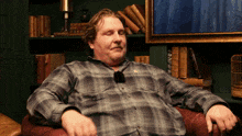 a man in a plaid shirt sits in a chair