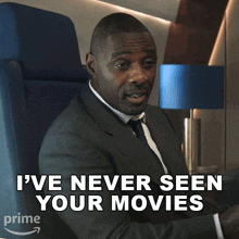 a man in a suit and tie is sitting in a chair with the words " i 've never seen your movies " behind him
