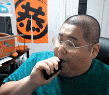 a man wearing glasses and a green shirt is smoking a cigarette in front of an orange sign that says go