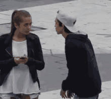 a man and a woman are standing next to each other on a sidewalk . the woman is holding a cell phone .