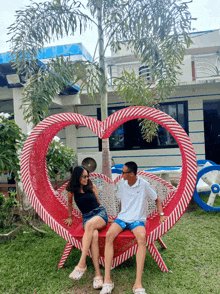 a man and woman sit on a heart shaped chair