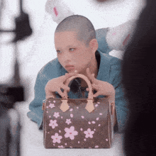 a woman with a shaved head is holding a louis vuitton bag with pink flowers on it