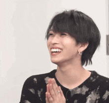 a young man wearing a black sweater is smiling with his hands folded
