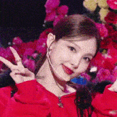 a close up of a woman wearing a red jacket and a microphone making a peace sign .