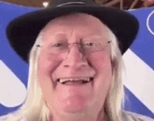 a man with long blonde hair is wearing a hat and glasses and smiling .