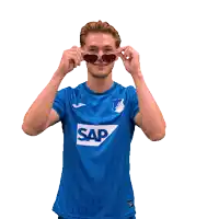 a man wearing sunglasses and a blue shirt with sap on it