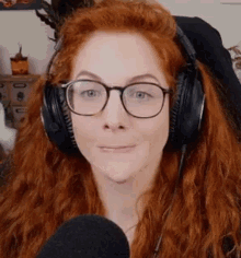 a woman with red hair and glasses is wearing headphones and looking at the camera .