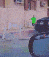 a man in a green shirt is walking down a street next to a car