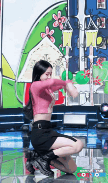 a woman in a pink crop top and black skirt is kneeling down on a stage with simply pop written on the bottom