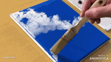a person is holding a brush over a blue canvas that says made in animatica on it