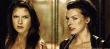 two women are standing next to each other and looking at each other in a dark room .