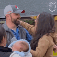 a man in a baseball cap is holding a baby while a woman looks on