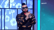 a man wearing sunglasses and red lipstick is standing in front of a sign that says sport 1