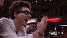 a man wearing sunglasses applauds during a basketball game in front of a banner for bamstore.com