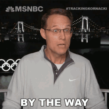 a man wearing glasses says by the way in front of a bridge