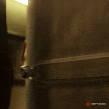 a woman peeking out from behind a door that says sony music on the bottom right