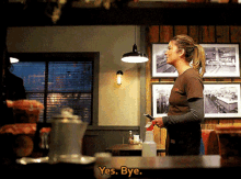 a woman in a brown shirt is standing in a restaurant and says yes bye