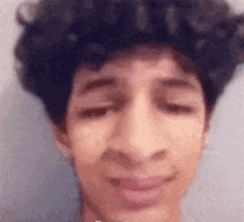 a close up of a young man with curly hair making a funny face with his eyes closed .