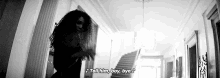 a black and white photo of a woman dancing in a hallway with stairs in the background .