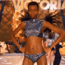 a woman in a bikini is walking down a runway in front of a sign that says victoria